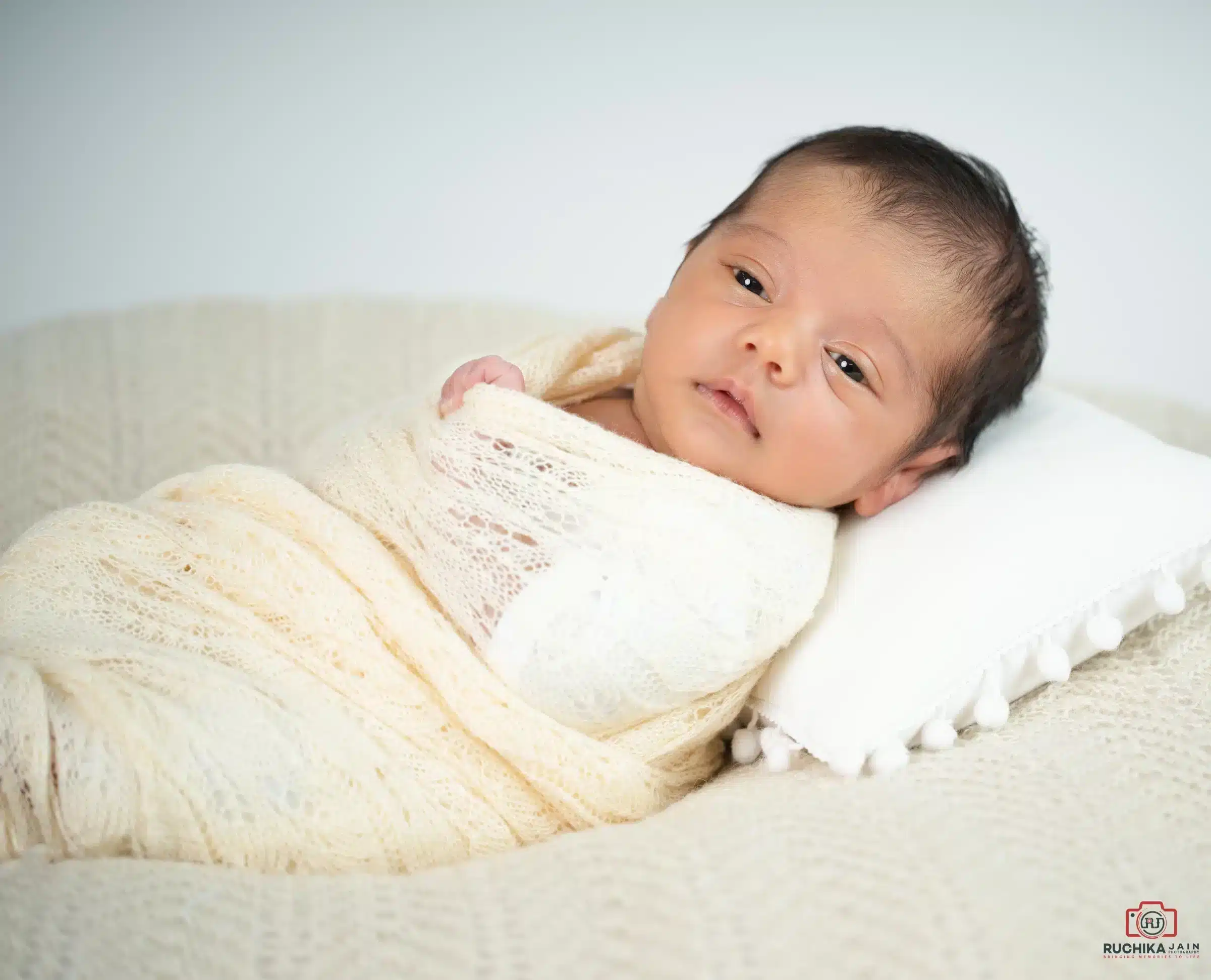 Newborn baby gently swaddled in a cream wrap during a serene professional newborn photoshoot in Wellington